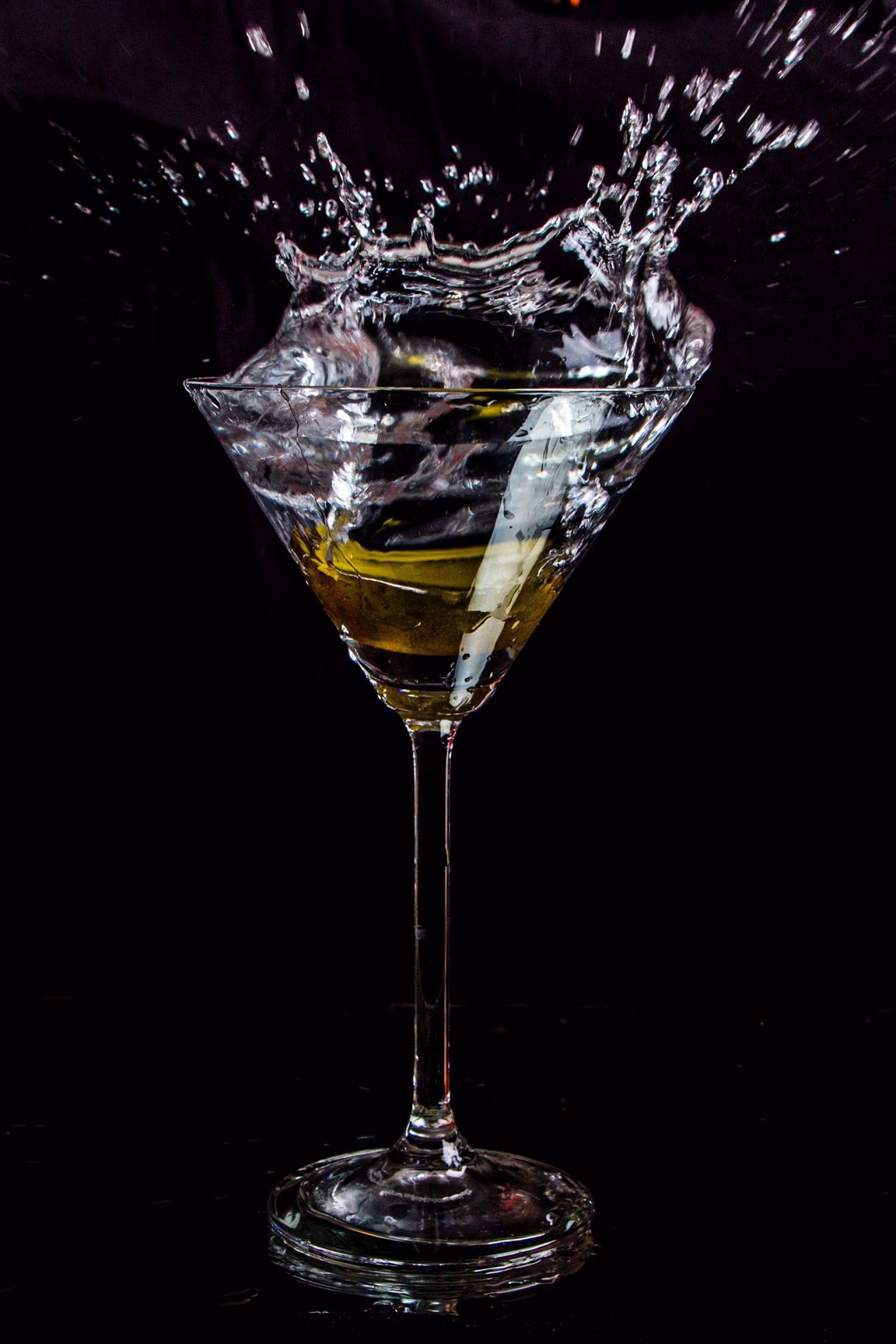 Cocktailglas met gele vloeistof en waterplons tegen zwarte achtergrond dry january actie en elegantie