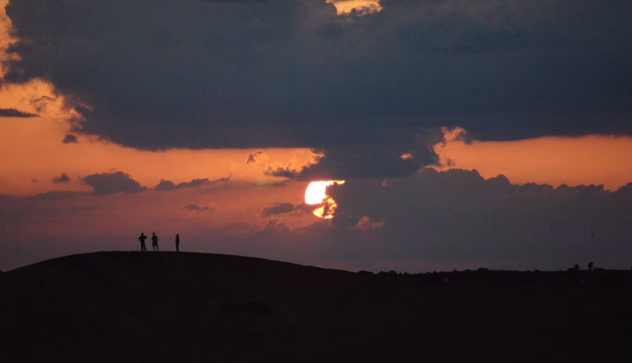 Rustgevend landschap bij zonsondergang met drie silhouetten op glooiende heuvel en oranje paarse hemel, titel Potdicht