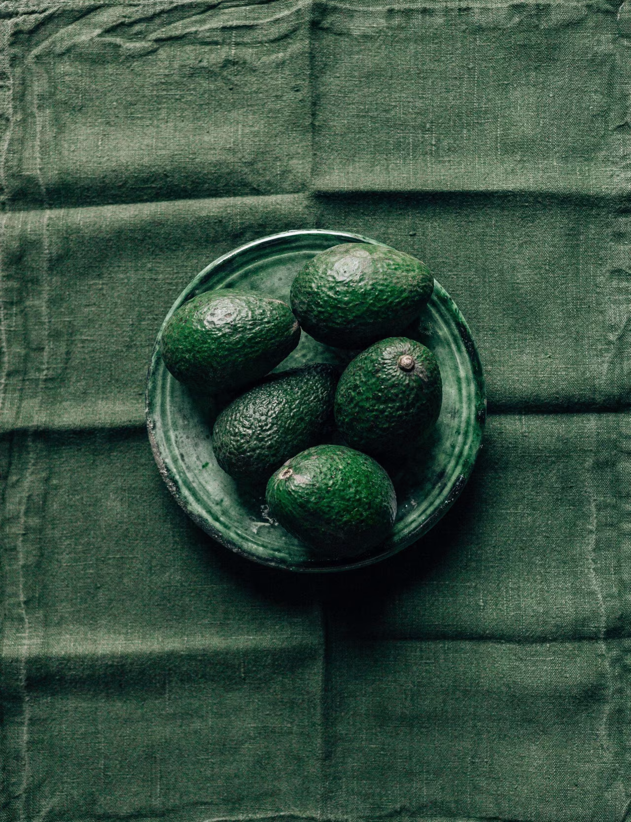 Bovenaanzicht ronde schaal met vijf avocado's op groene achtergrond natuurlijke gezonde voeding tips