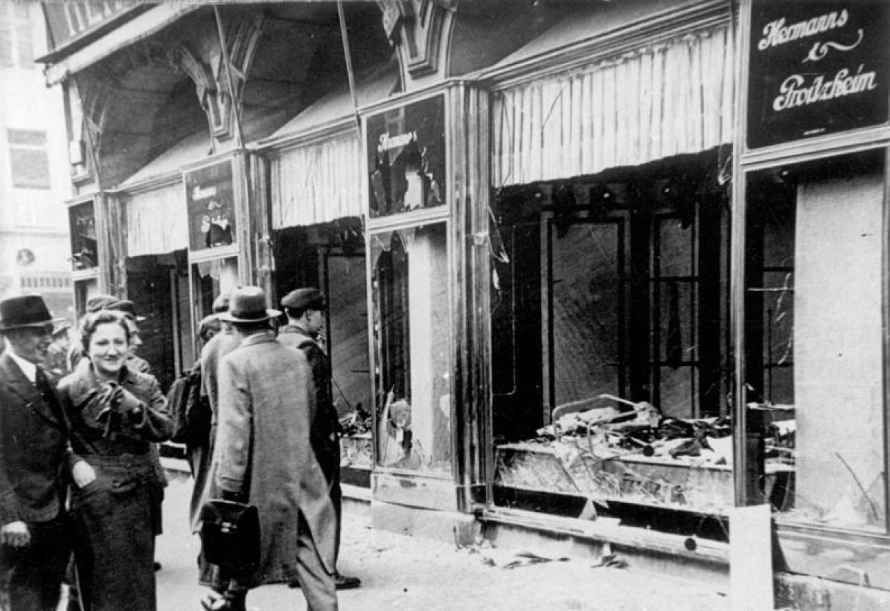 Zwart-wit straatbeeld met gebroken winkelruit Asman & Friedländer tijdens Kristallnacht herdenking, opstaan tegen onrecht en intolerantie