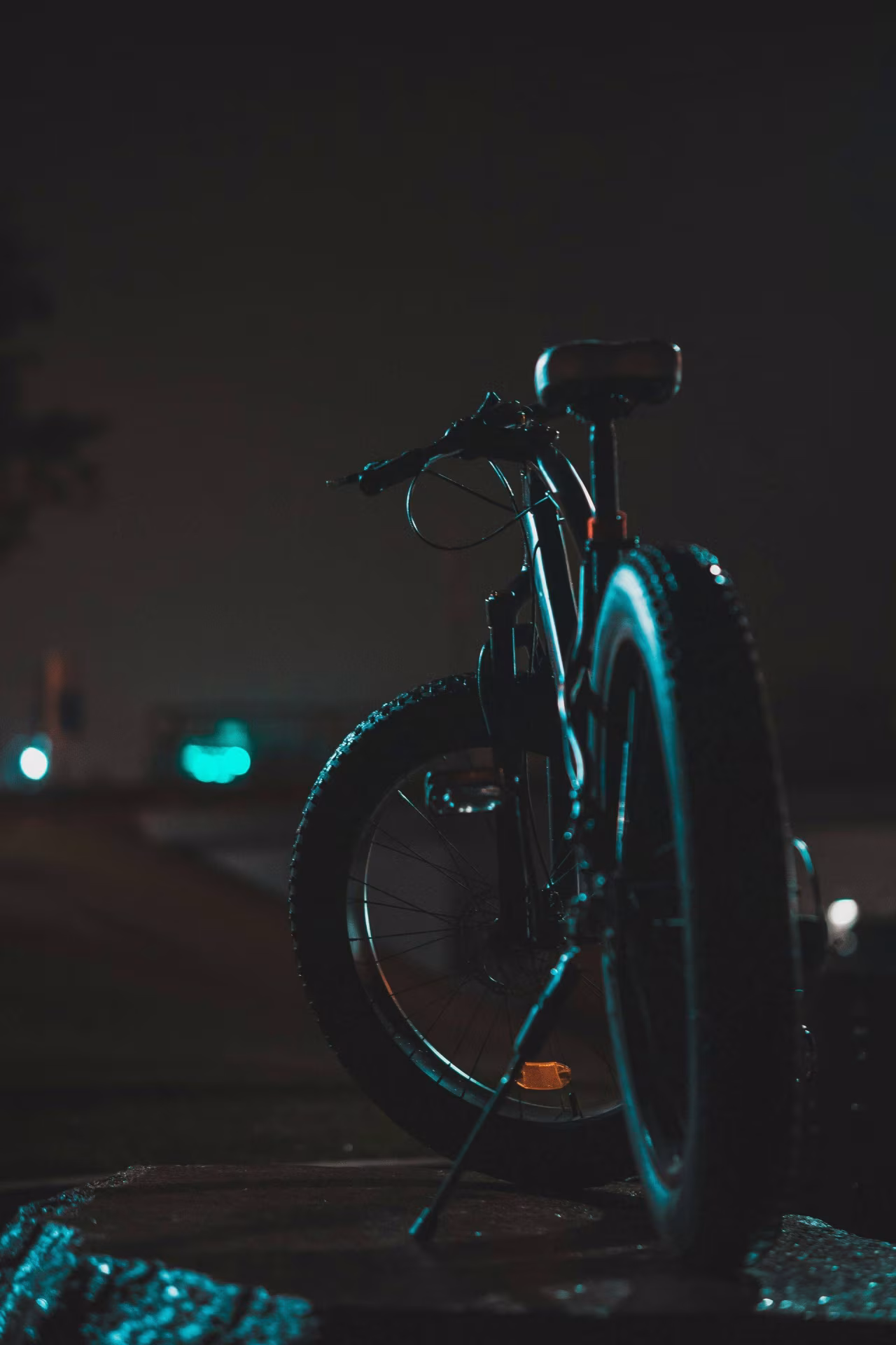 Oversteek: nachtelijk beeld van een geparkeerde fiets met focus op achterwiel en zadel op betonnen ondergrond