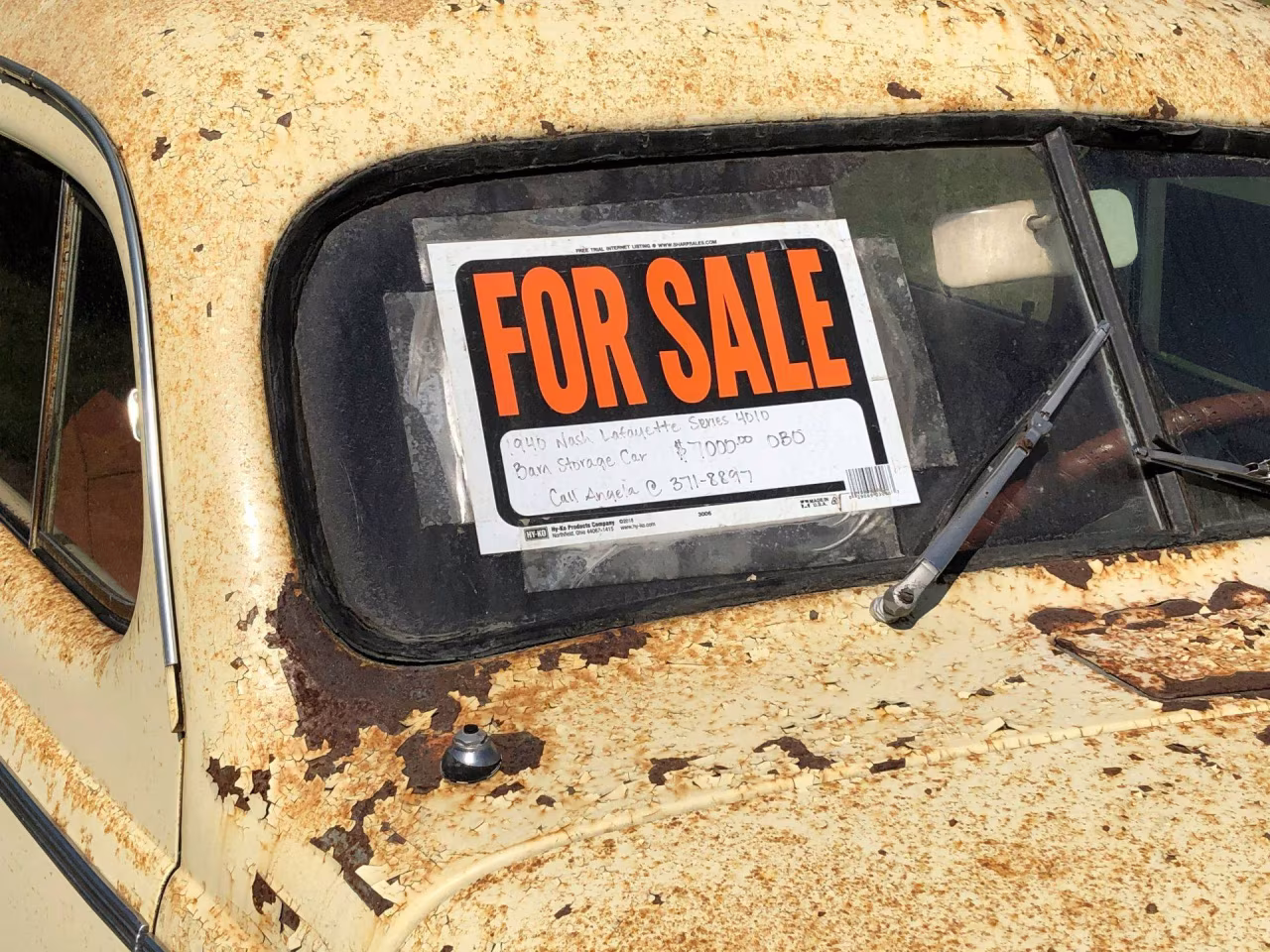Raam met te koop bordje for sale met handgeschreven verkoopinfo en roestig voertuig h2 handel tkk