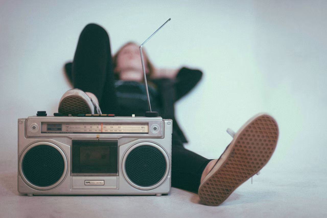 Radio-cassette speler met antenne en grote speakers op de voorgrond, persoon ligt ontspannen op de achtergrond, nieuwsoverzicht van 24 t/m 30 juni 2024 over Brexit, Dagestan aanslagen, Mekka bedevaart, inkomens, natuurbranden, Krim conflict, huurwetten, EU topbanen, Kenia protesten, toeslagenschandaal, radio populariteit, overheid rechtszaken, EK voetbal, Oranje optimisme, Filippijnen China conflict