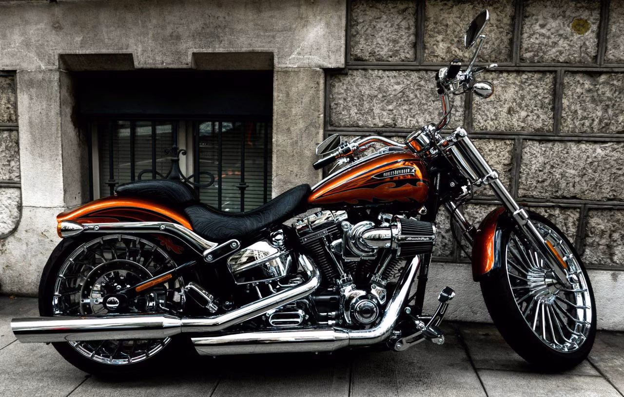 Foto van een robuuste oranje-bruin-zwarte HARLEY-DAVIDSON motorfiets met glanzende chromen onderdelen geparkeerd tegen een stenen muur, bij Nieuws overzicht 22-28 april 2024