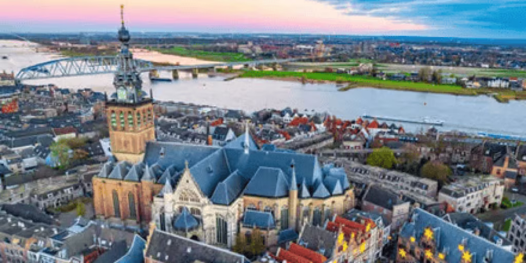 Tijdloos uitzicht over Nijmegen met de Stevenskerk en Waalbrug bij zonsondergang vanuit Valkhofpark