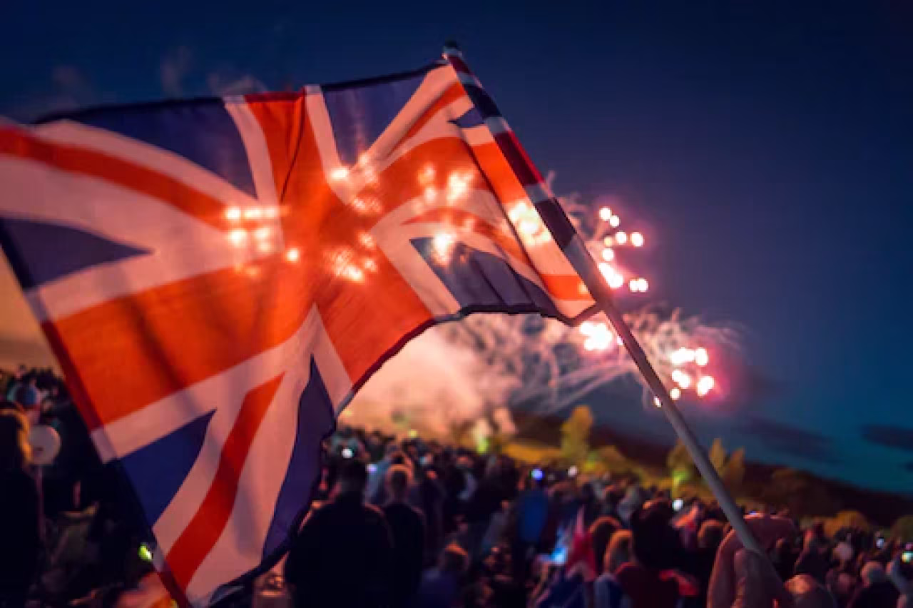 Vlag van het Verenigd Koninkrijk omhoog gehouden met vuurwerk op de achtergrond tijdens feestelijke buitenbijeenkomst nieuwsoverzicht 12 t/m 18 dec 2022