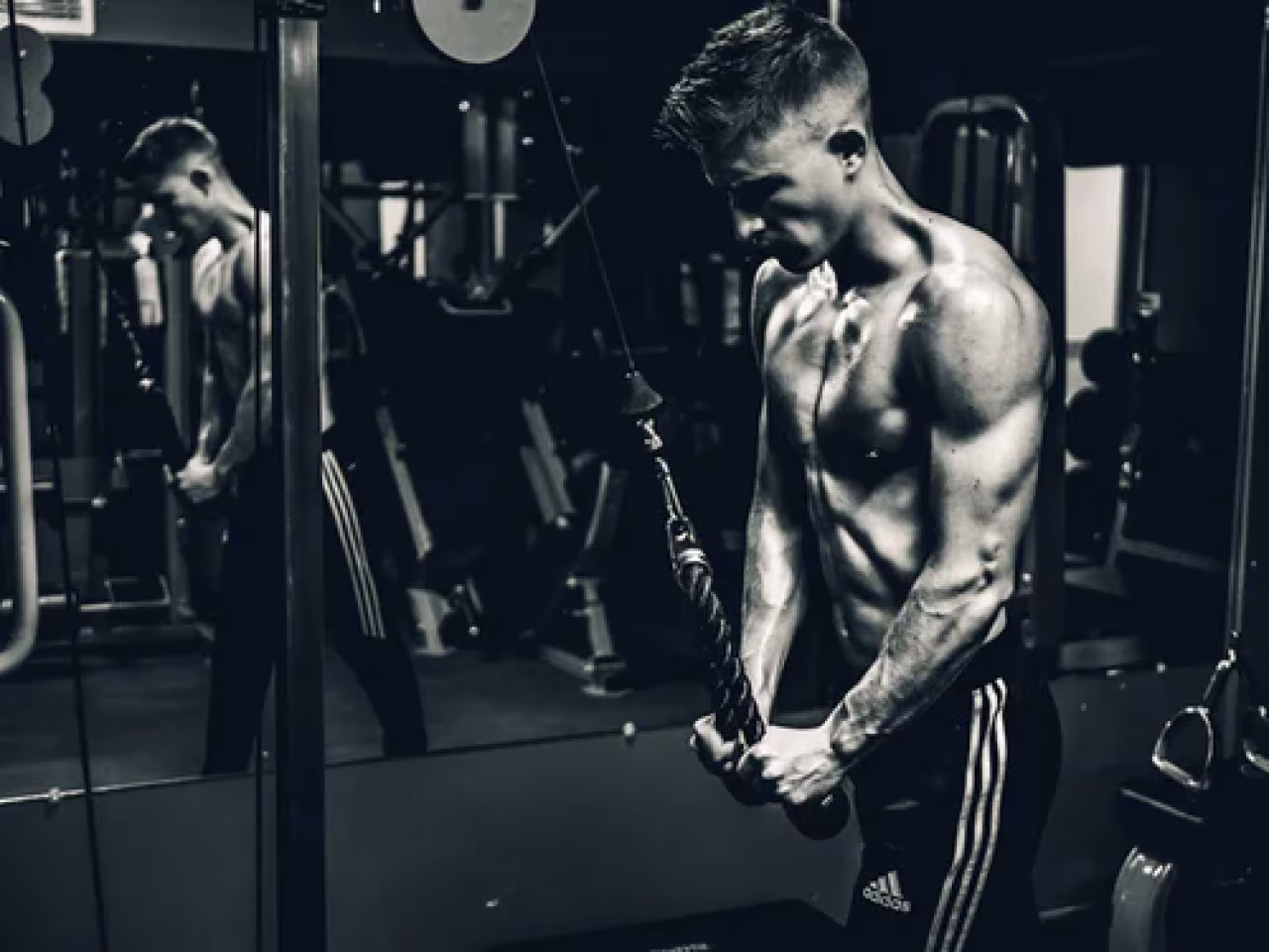 Gespierde sporter doet tricep pushdown oefening in sportschool met kabelmachine, thema Gezond is het nieuwe rijk