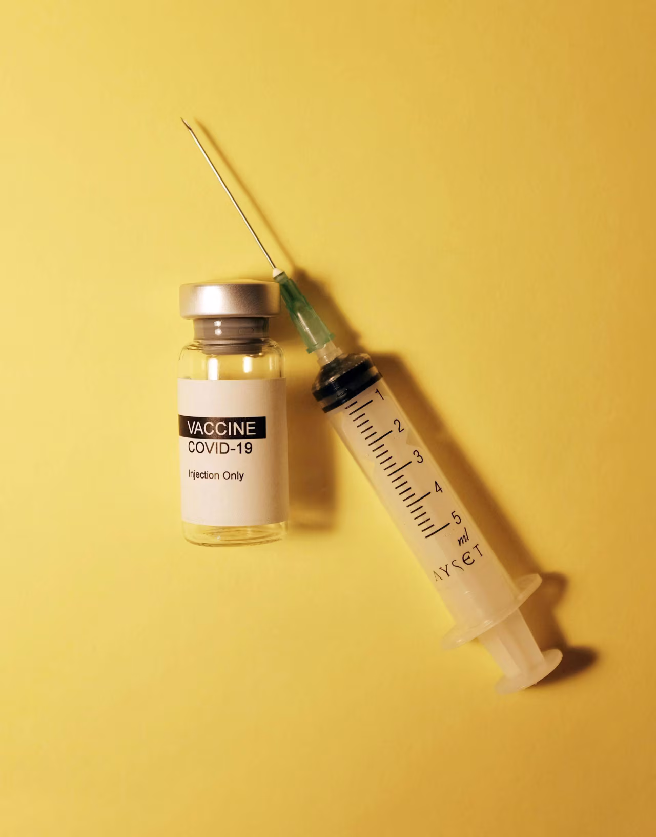 Afbeelding met een flesje gelabeld VACCINE COVID-19 en injectiespuit voor Oversterfte in de coronajaren zat vooral bij niet-gevaccineerden