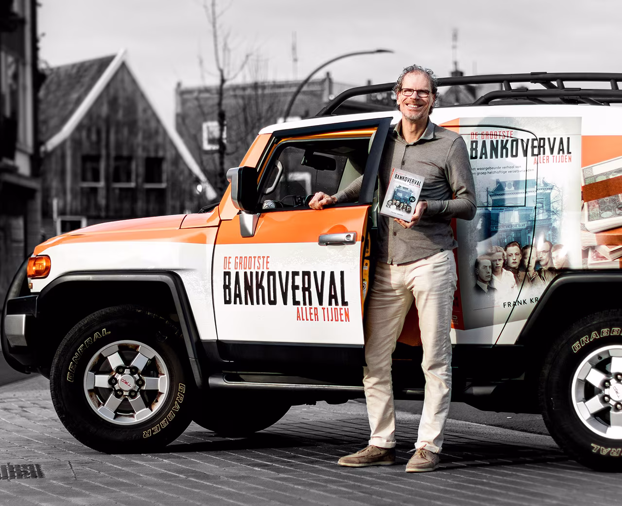 Promotie van boek de grootste bankoverval aller tijden met Frank Krake lachend in de deuropening van oranje-witte auto