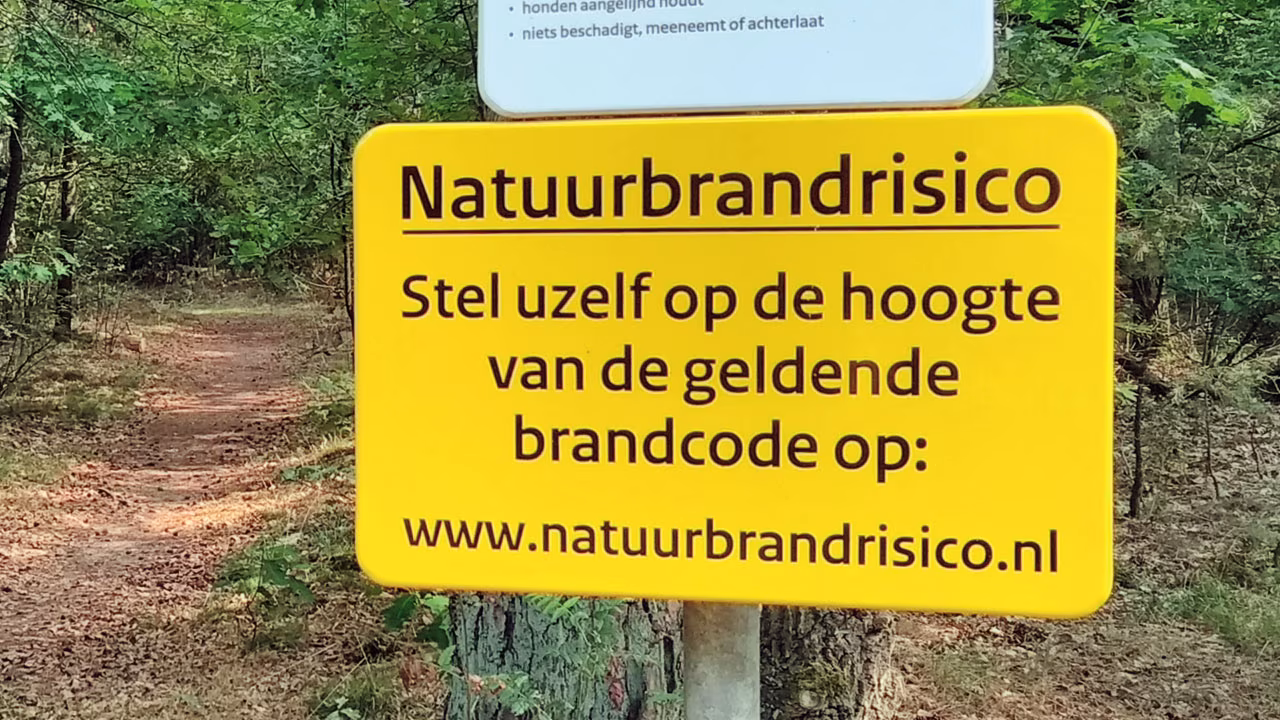 Waarschuwingsbord natuurbrandrisico langs bospaadje met tekst natuurbrandrisico en www.natuurbrandrisico.nl, regionaal nieuwsoverzicht