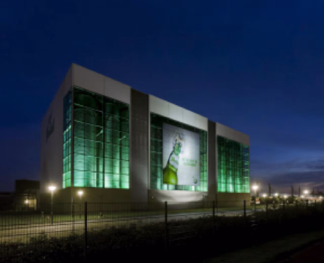 Gebouw met groot reclamebord van groene bierfles en flesopener, nachtelijke verlichting in context grolsch betaalt miljoenen euro's loonsteun niet terug