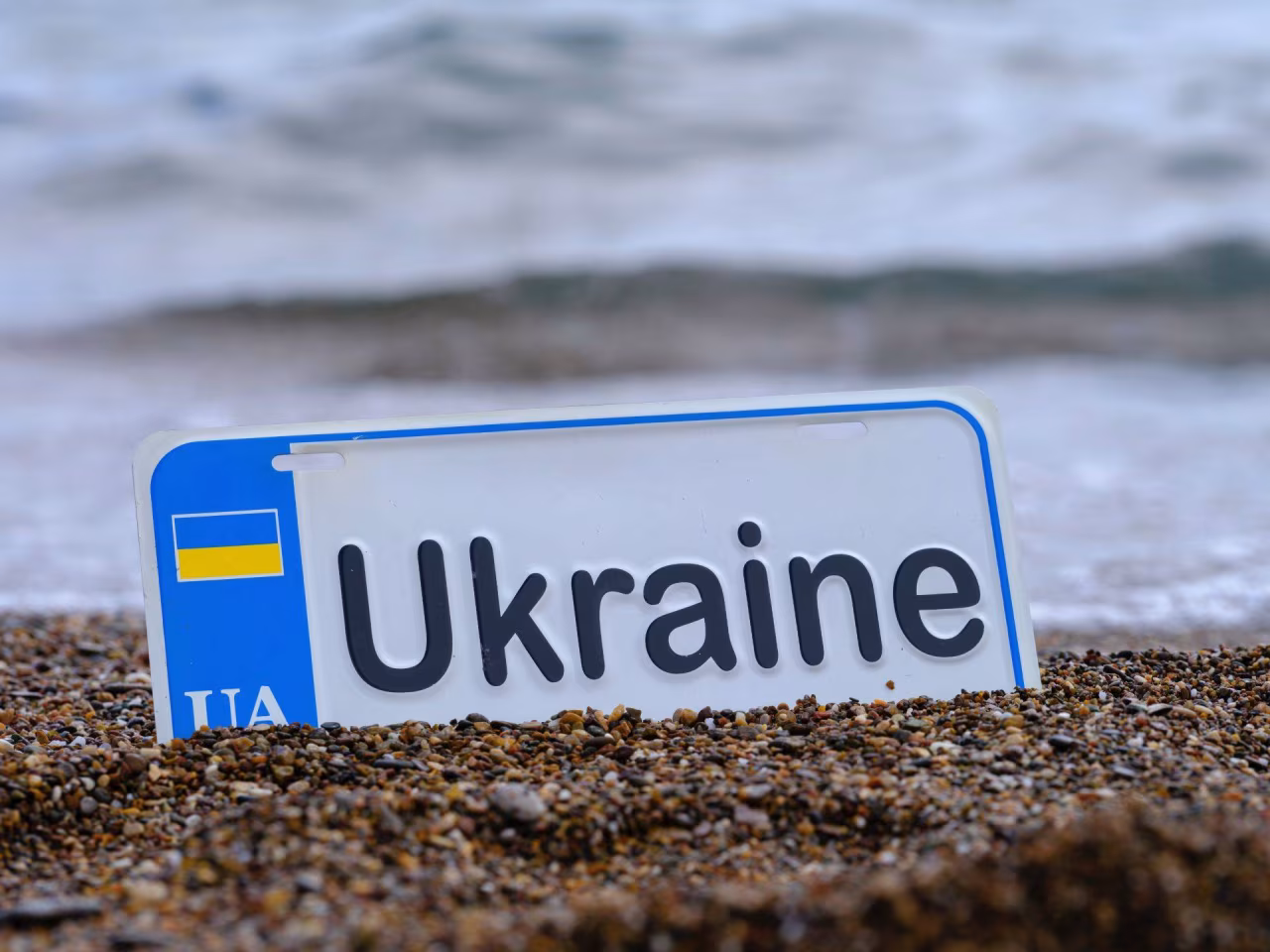 Kentekenplaat Ukraine met blauw-gele UA vlag in zand aan zee, thema De oorlog in Oekraïne van ma 16 oktober t/m zo 22 oktober 2023