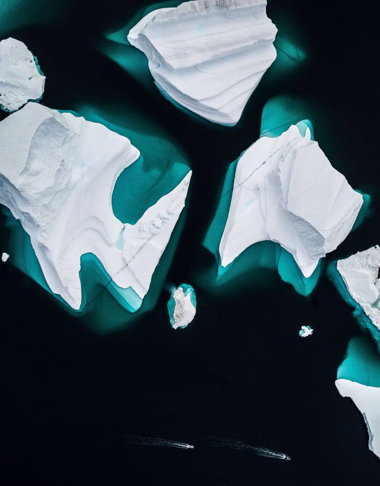 Luchtfoto van grote ijsbergen in donkerblauw water met twee boten in beweging rond de zuidpool, weinig zee-ijs deze winter