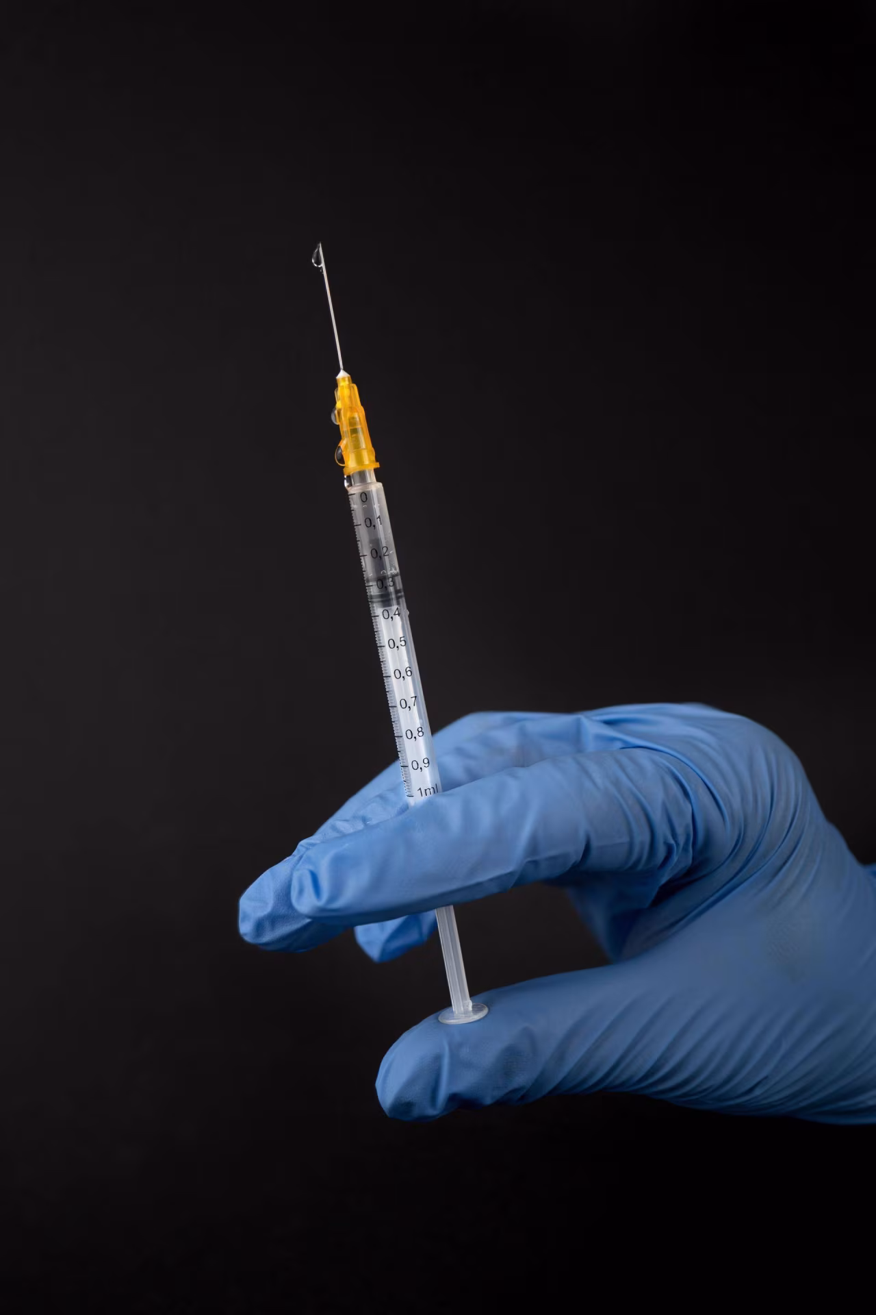 Hand met blauwe medische muts houdt spuit met druppel vloeistof vast voor Europese vaccinatie top tien artikel over vaccinaties