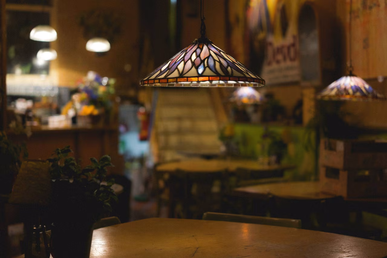 Gezellig café interieur met Tiffany-stijl lamp, houten tafels, Perzische kleedjes en authentieke sfeer in Venster, Twents mediaplatform TKKR.