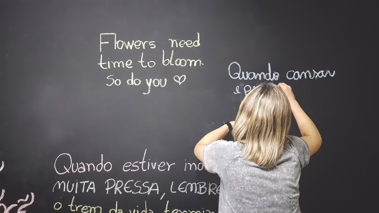 Moerstaal bordtekst met 'Flowers need time to bloom so do you ♥' en Portugese woorden geschreven met krijt als inspiratiemotivatie