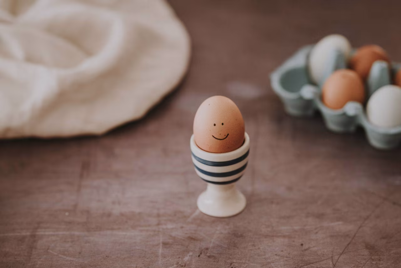 Ei met glimlach in eierdopje op houten tafel naast eierdoos, afbeelding bij Oma en homeopaat in één TKKR