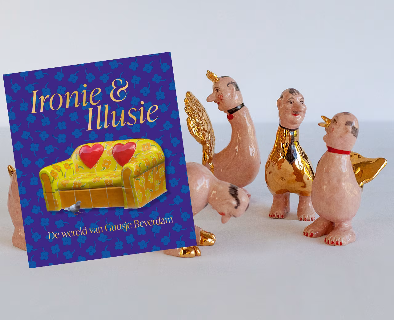 Boek Ironie & Illusie met titel De wereld van Guusje Beerdam en kleurrijke beeldjes met menselijke gezichten en dierlijke lichamen