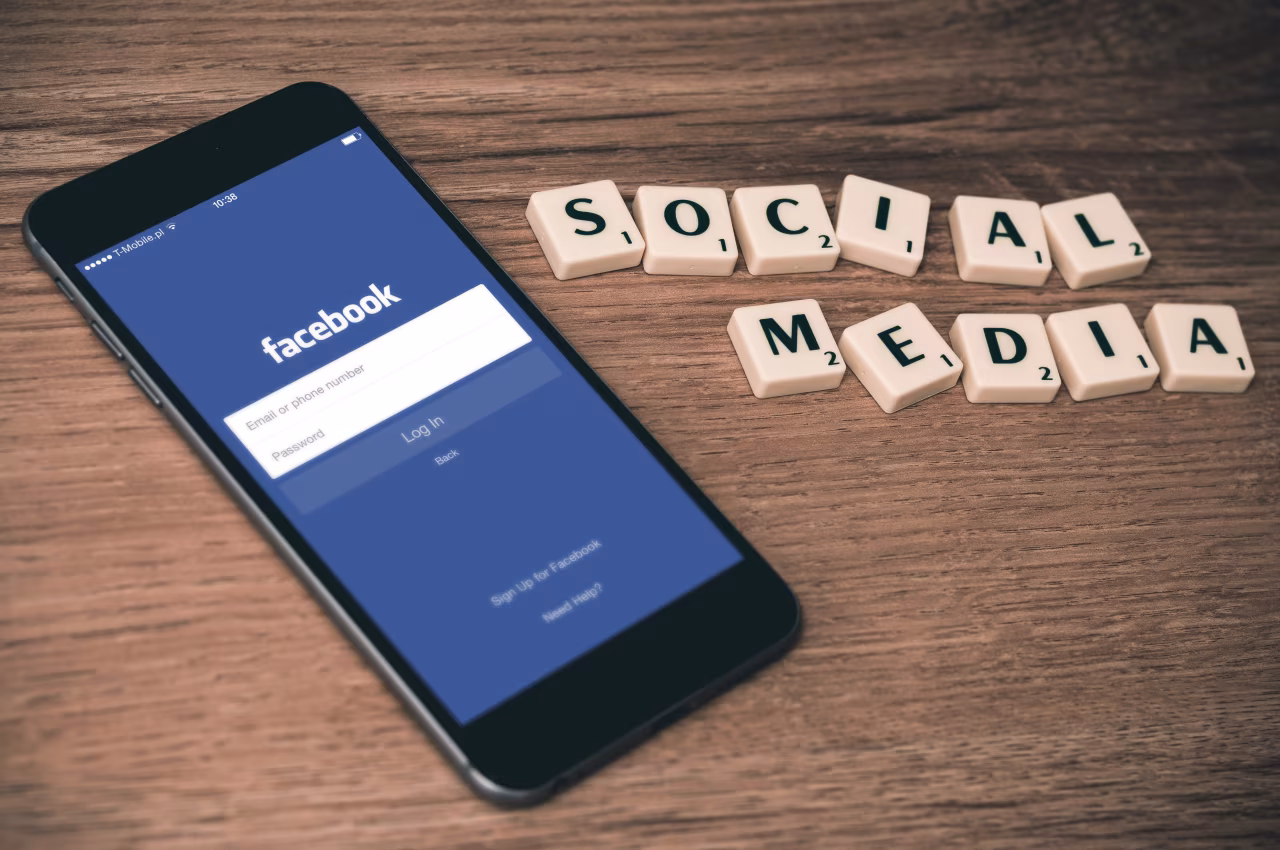 Smartphone met Facebook inlogscherm op hout, omringd door houten blokjes met letters SOCIAL MEDIA, thema De realiteit van de feiten en die van de meningen