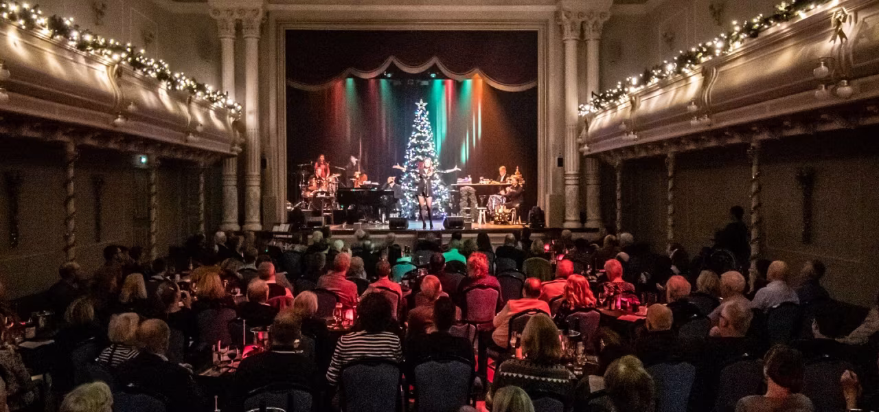 Willems Kleine Kerst middagvoorstelling met kerstboom op podium, muzikanten en publiek in feestelijk versierde theaterzaal