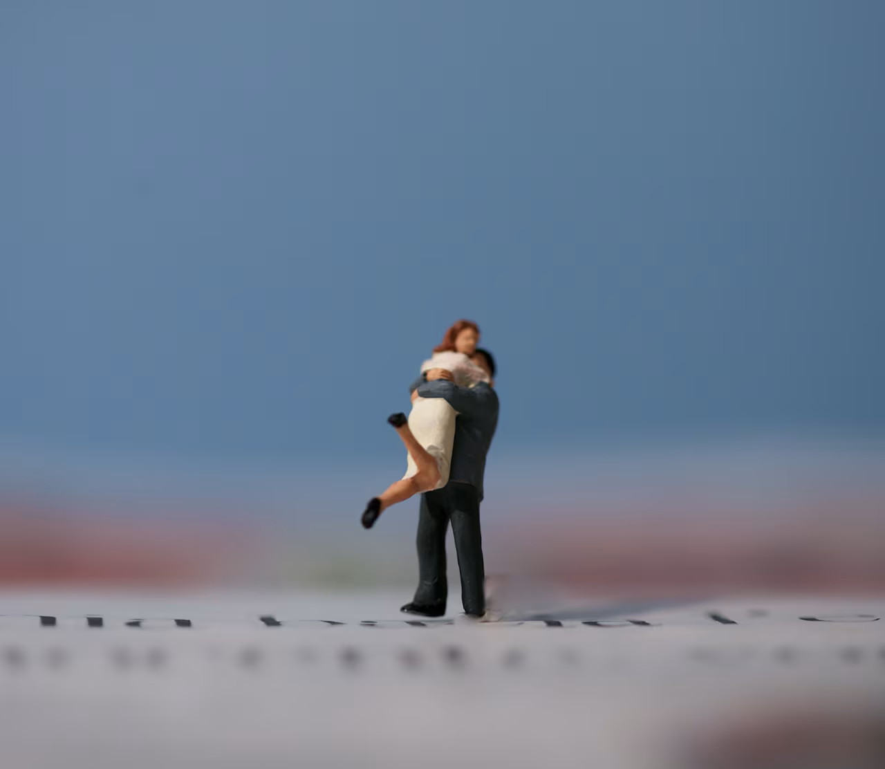 Kleine schaalmodel-sculptuur van twee figuren die een omhelzing vormen, symbolisch samenzijn en liefde, achtergrond lichtblauw naar roze