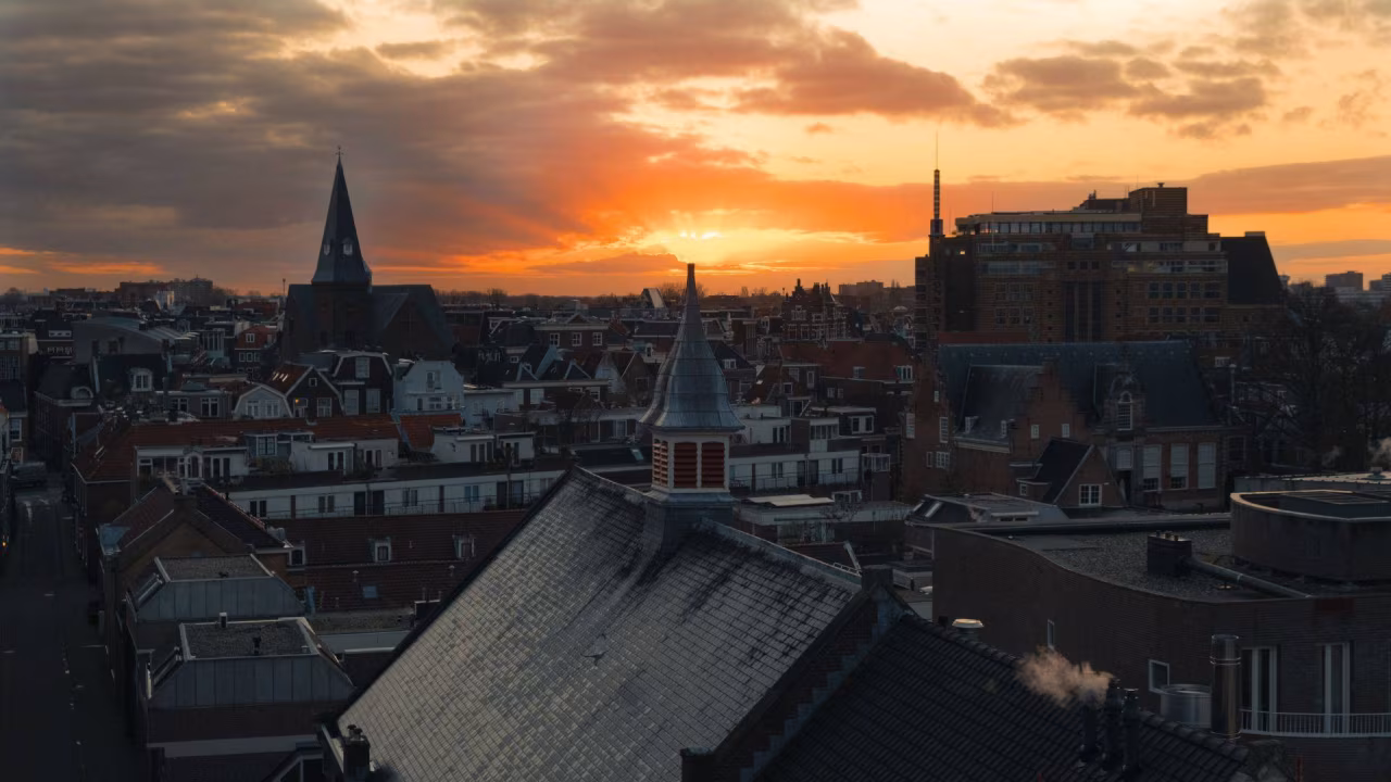 Stadsgezicht bij zonsondergang met oranje en gele lucht en kerktoren zichtbaar in rustige stedelijke omgeving verlichting