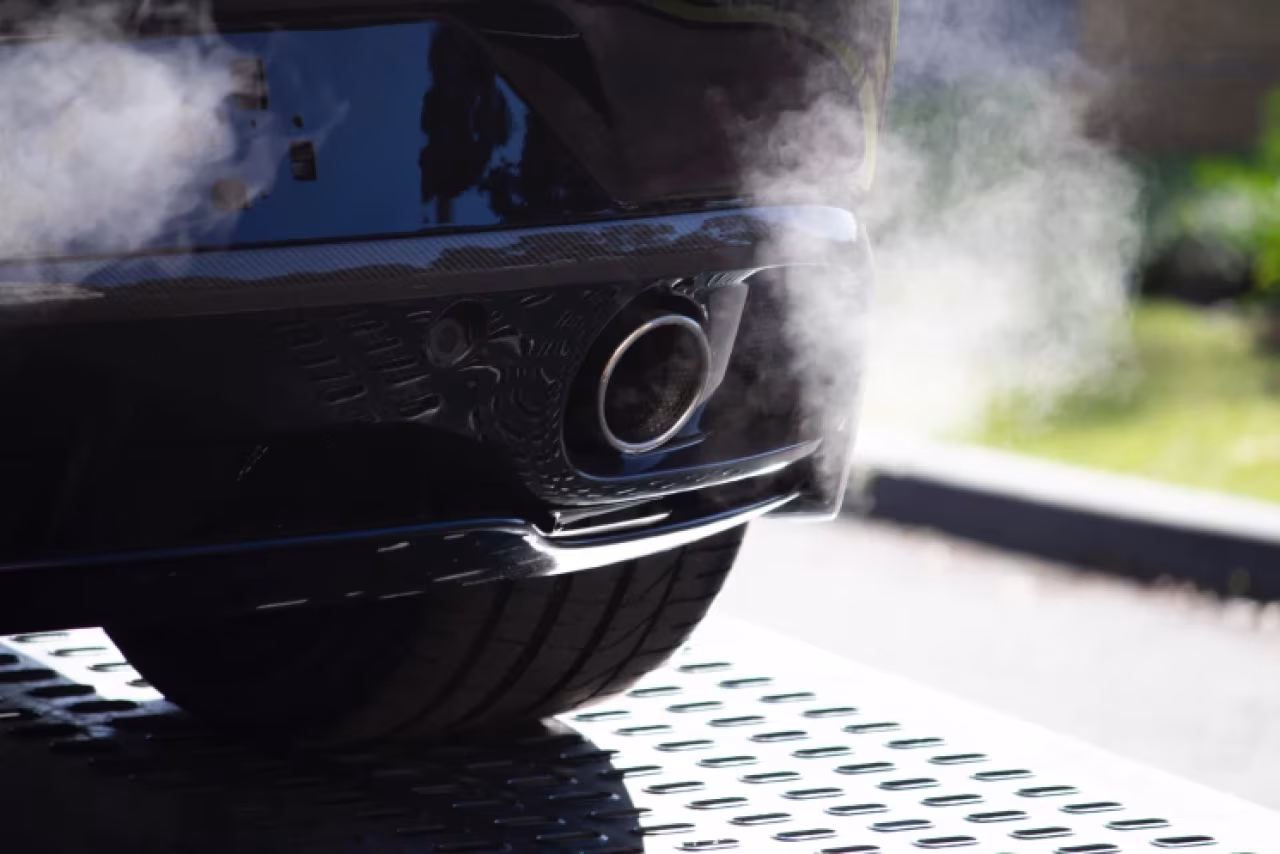 Close-up van een auto-uitlaat met witte rook op metalen rooster, focus op motoruitstoot in autotechniek en milieueffecten - nieuwsoverzicht