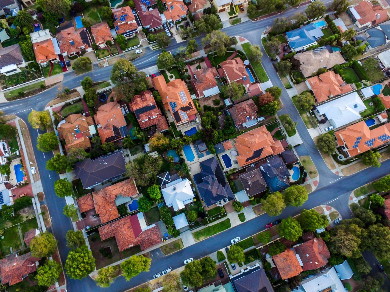 Luchtfoto van een groene woonwijk met diverse huizen, daken en zwembaden, overzicht woonstructuur januari 2024