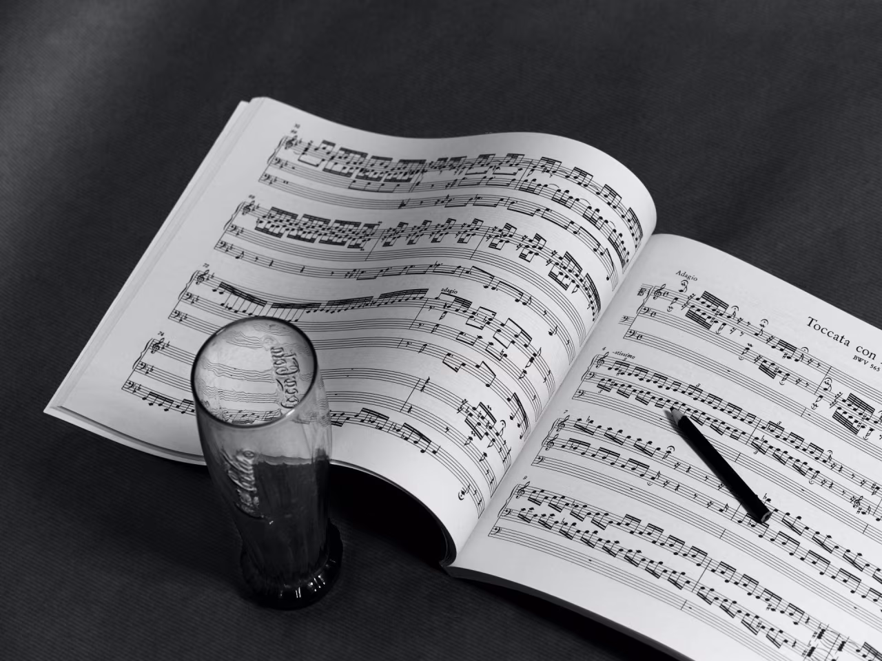 Zwart-wit foto van bladmuziek Toccata met muzieknoten, pen en glas die noten vervormt bij artikel Hoe Bach botst met paard in de gang