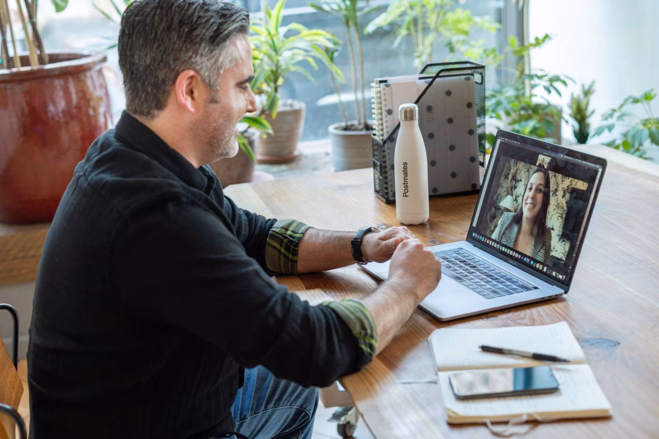 Binnenruimte met laptop en videovergadering, houten tafel met notitieboekje, waterfles en smartphone zichtbaar. Nieuwsoverzicht 25 sep t/m 1 okt 2023 benadrukt online communicatie.