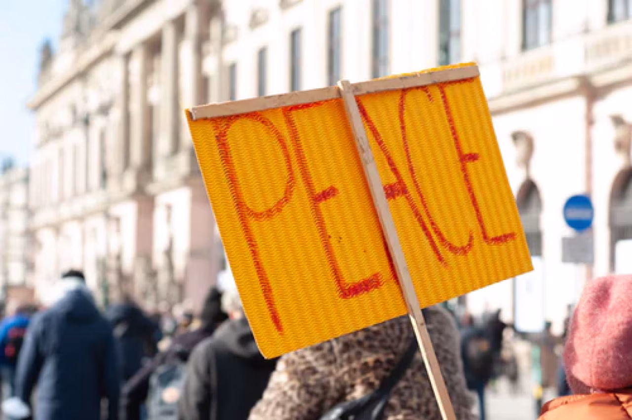 Bord met rode letters PEACE vastgehouden tijdens vredesdemonstratie op straat in stedelijke omgeving, De Oorlog in Oekraïne
