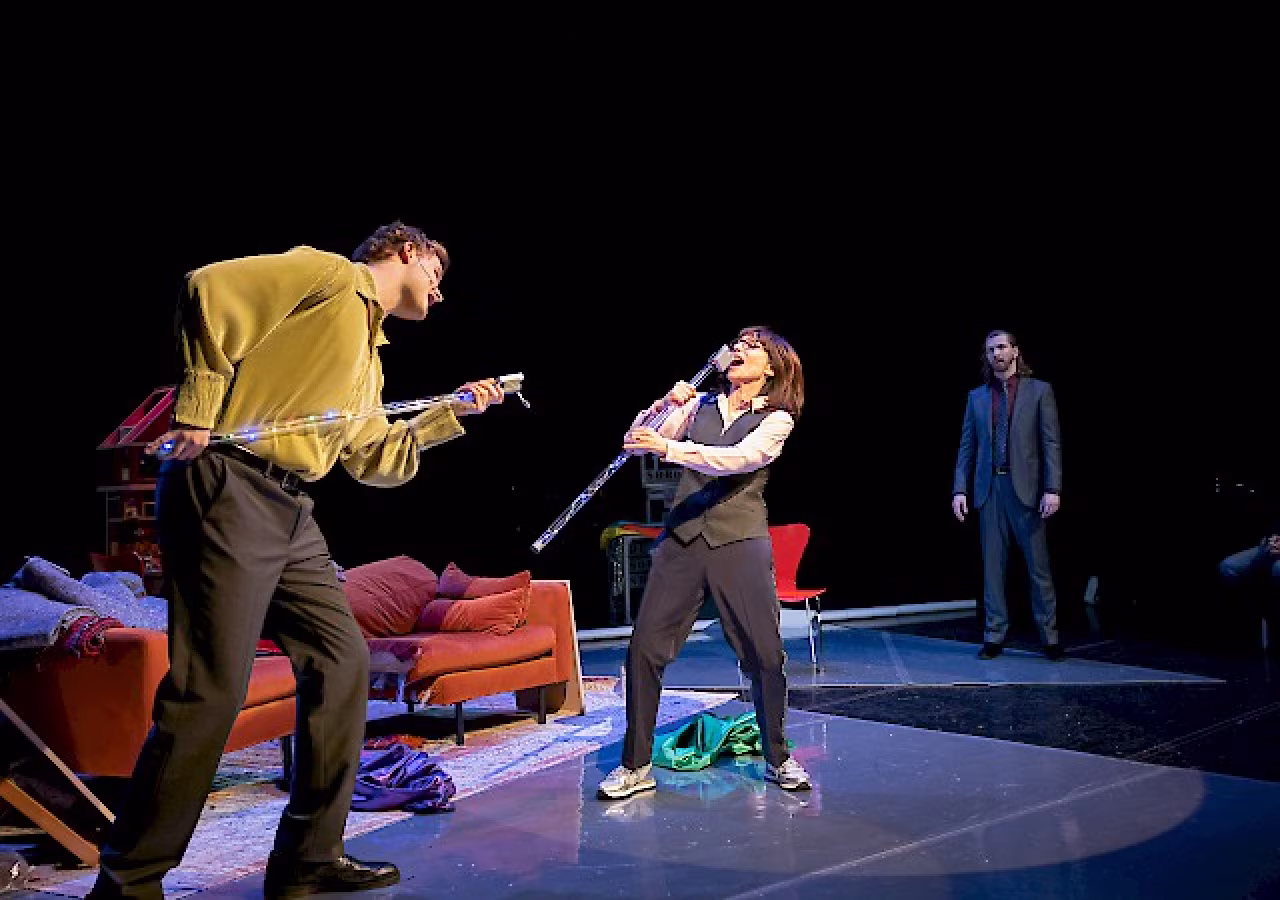 Podiumfoto theatervoorstelling The Making of Soros the Musical met acteurs, staf en rood bankstel, scène leven George Soros