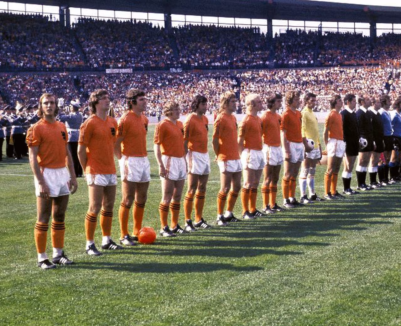 Voetbalteam in oranje en wit op grasveld in vol stadion voor aanvang WK 1974 theatercollege over totaalvoetbal en finale