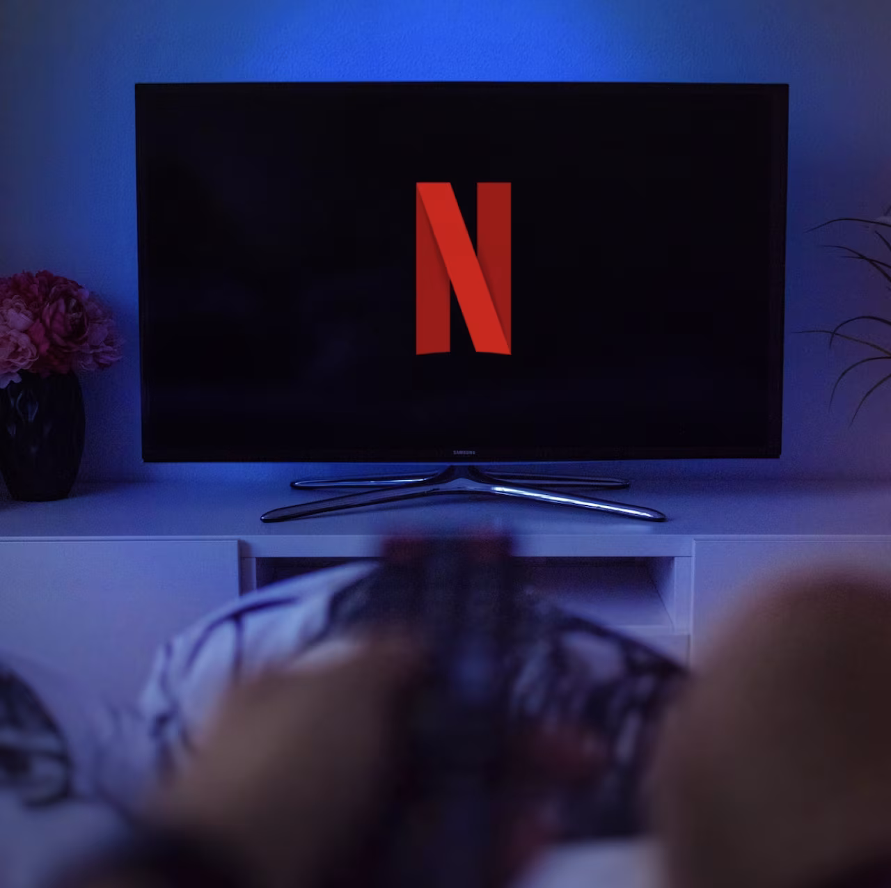 Netflix wachtwoord delen gaat geld kosten toont Netflix logo op tv in donkere kamer met blauwe gloed