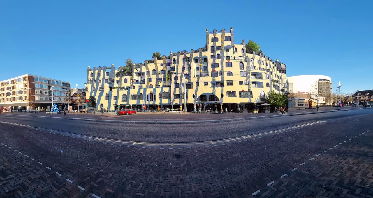 Hundertwasser in Hengelo toont uniek golvend geel gebouw met zwarte lijnen, groene daktuinen en brede straat met tramrails