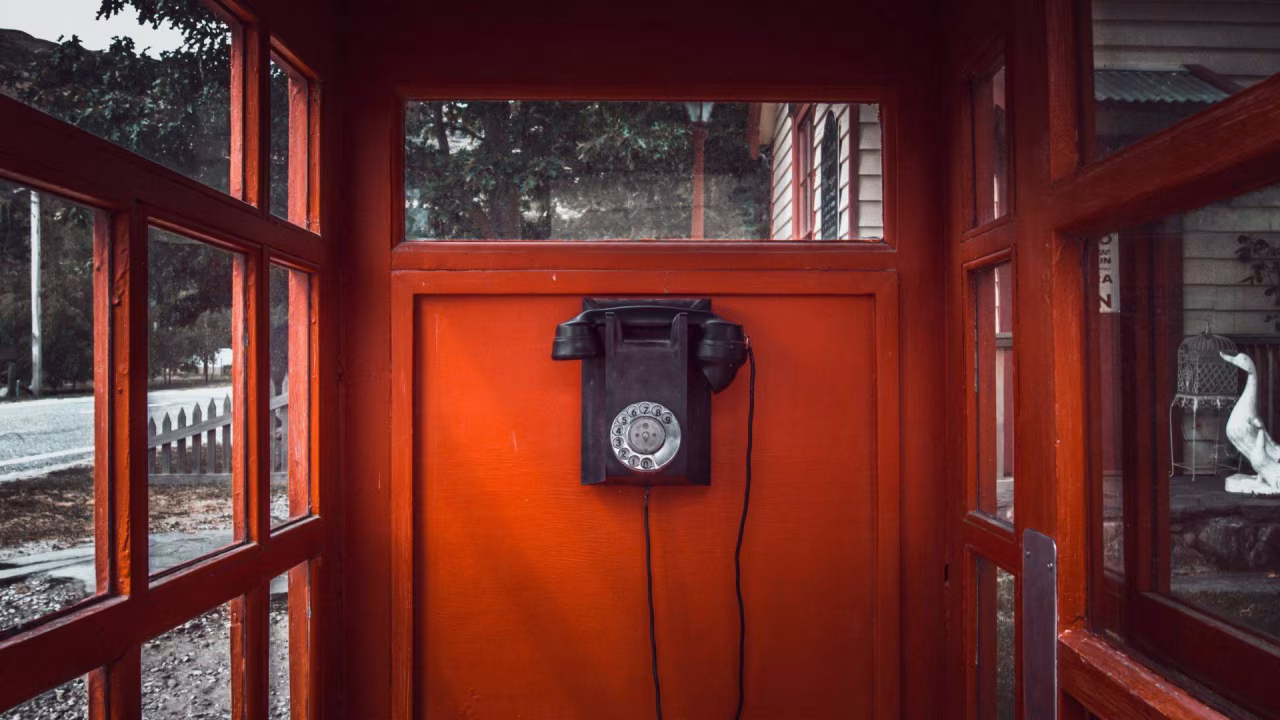 Een oranje houten telefooncel met oude draaitelefoon en eend beeld buiten, thema verouderde communicatie