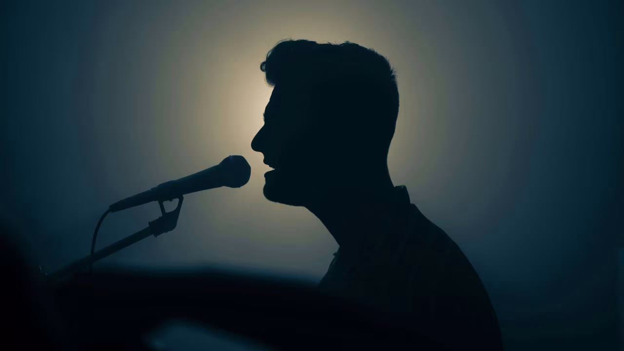 Silhouet van een zingende persoon bij een microfoon met licht van achteren, illustratie bij auditie op tkkrs website over twente