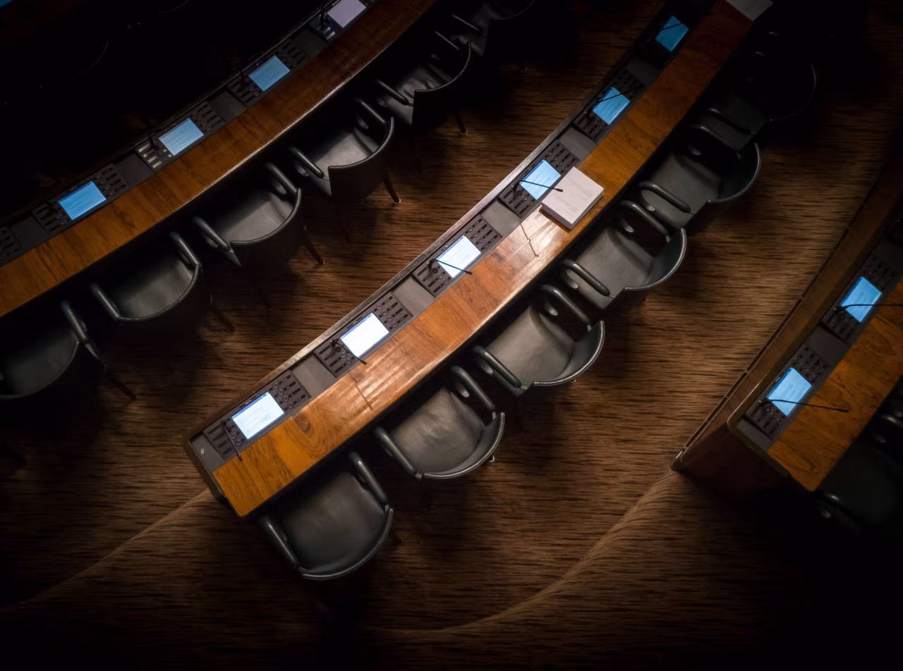 Bovenaanzicht zaal met halfronde houten tafels en stoelen, geschikt voor formele bijeenkomsten volgens nieuwsoverzicht TKKR