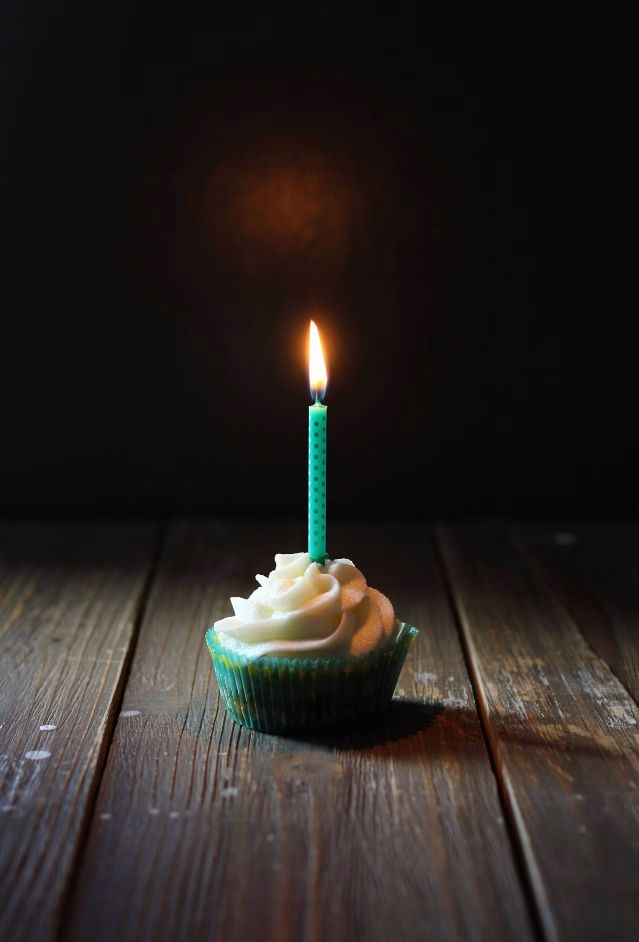 Eenzame cupcake met witte glazuur en een brandende groene kaars met zwarte stippen op houten oppervlak, thema Verjaring