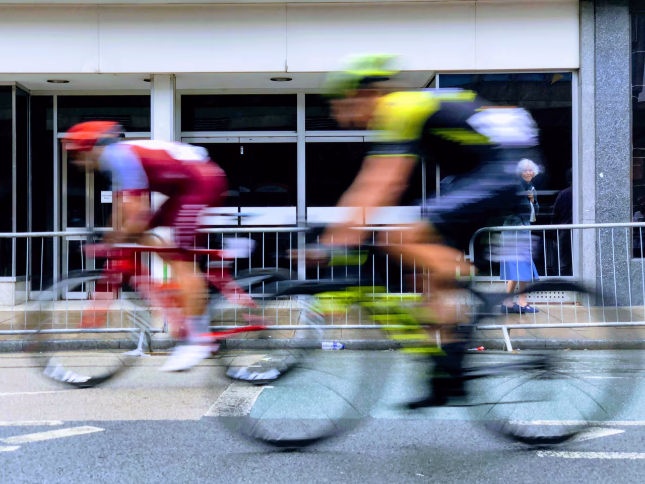 Snel bewegende fietsers in stedelijke omgeving met hek, ramen en grijze gevel toont sportoverzicht van 14-20 februari 2022 tkkr