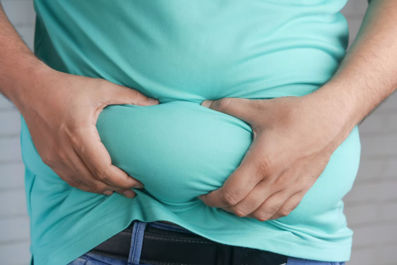 Close-up van handen die buik indrukken, thema ernstig overgewicht, obesitas, twents mediaplatform over overgewicht in nederland
