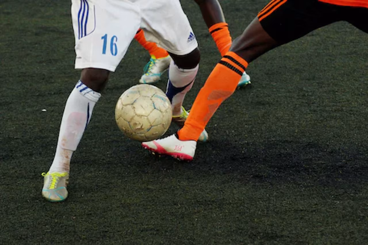Close-up voetbalactie met spelers benen en bal op donker kunstgrasveld tijdens zelfs voetbal is oké