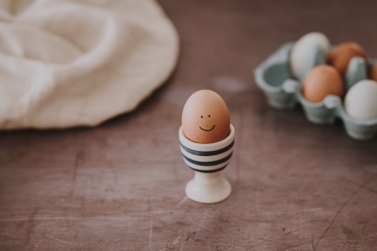 Ei met glimlach in eierdopje op houten tafel naast eierdoos, afbeelding bij Oma en homeopaat in één TKKR