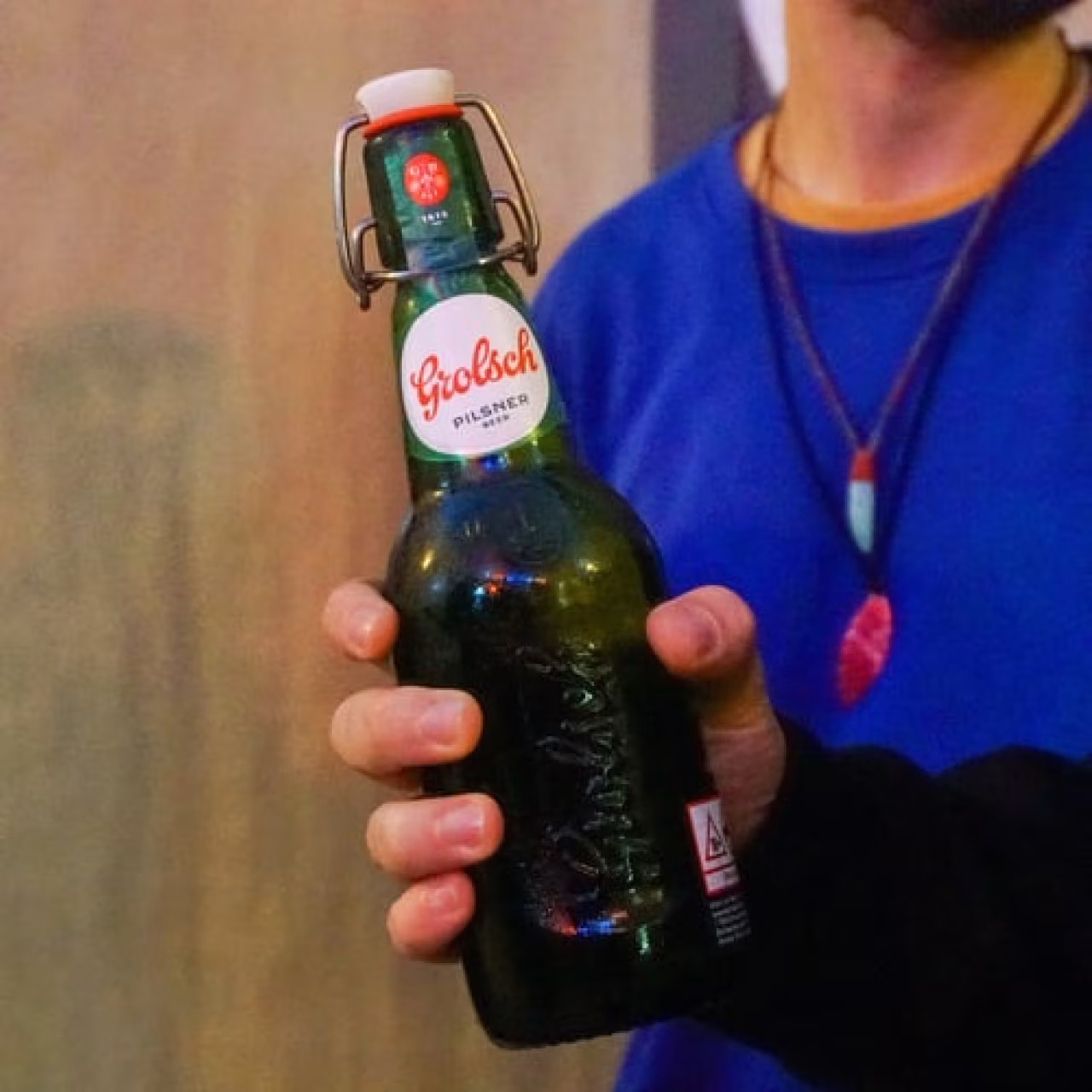 Regionaal weekoverzicht met een hand die een groene Grolsch Pilsner fles vasthoudt, sfeer van ontspanning