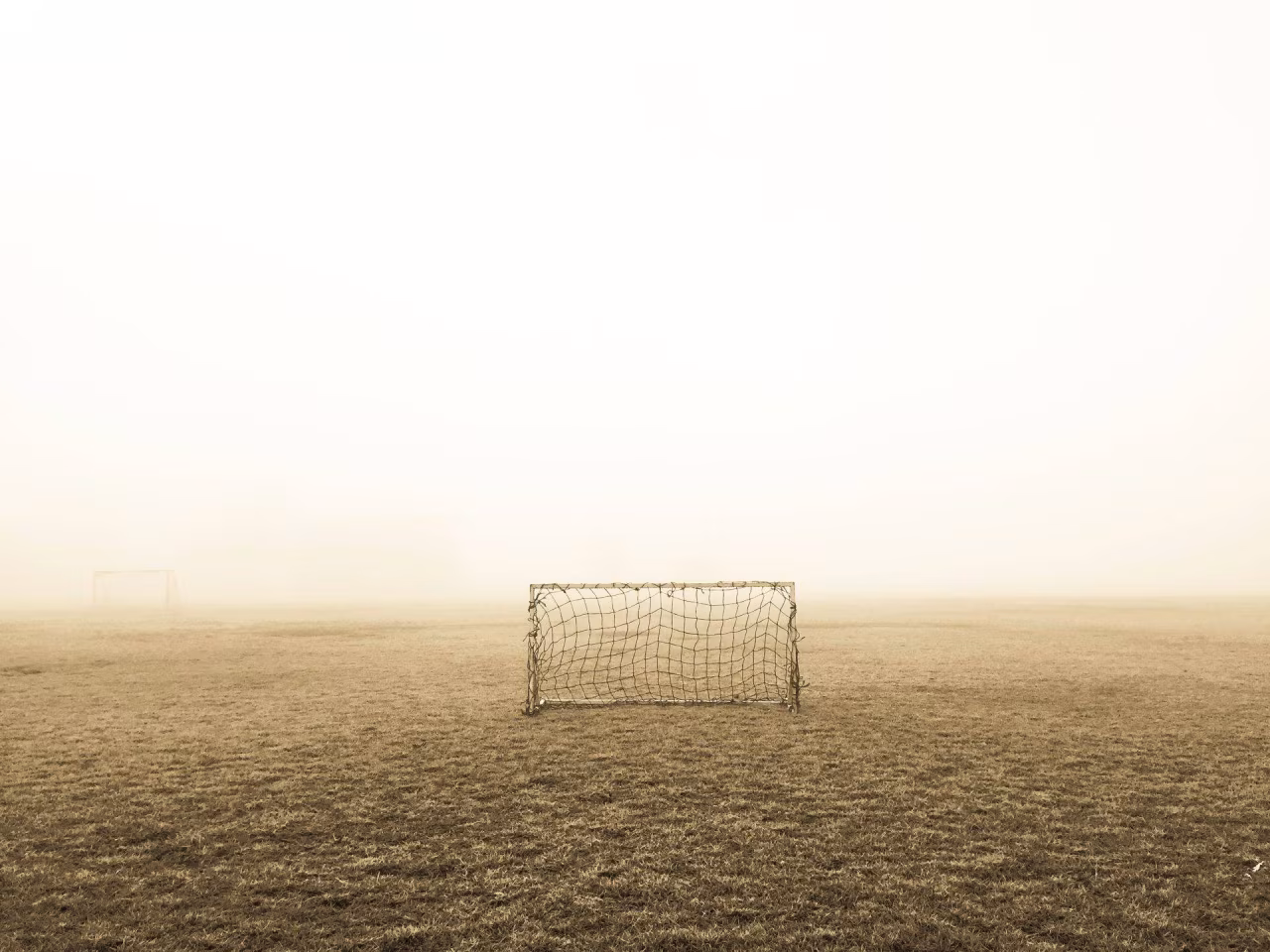 Voetbaldoel op groot leeg veld in lichte mist bij artikel 'zijn twee palen wel genoeg voor oudere doelman?'