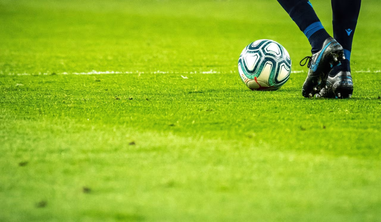Sportoverzicht maart 2022: voet op voetbal met noppen op groen veld, moment van balcontact in voetbalwedstrijd