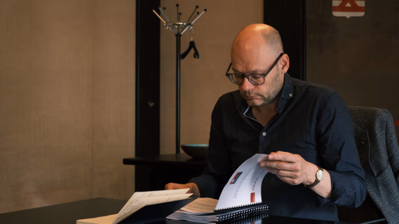 Interieurfoto met persoon aan bureau lezend in documenten in studieomgeving, thema 'aanzet tot dialoog van onderop over toekomst van twente'