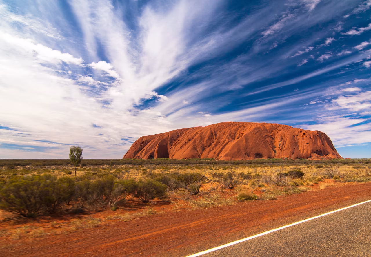 Eenzaam maar niet alleen: Uluru en de Kroezeboom in Australië met rode rotsformatie en blauwe lucht