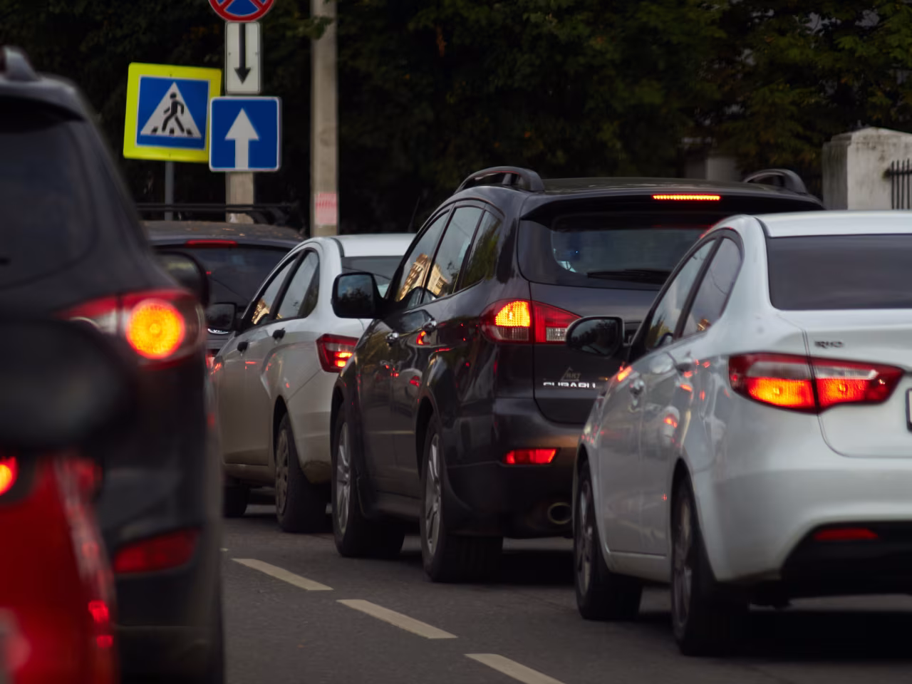 In de file op weg naar oude normaal met vijf auto's en brandende remlichten bij verkeersborden zebrapad en pijl rechtdoor