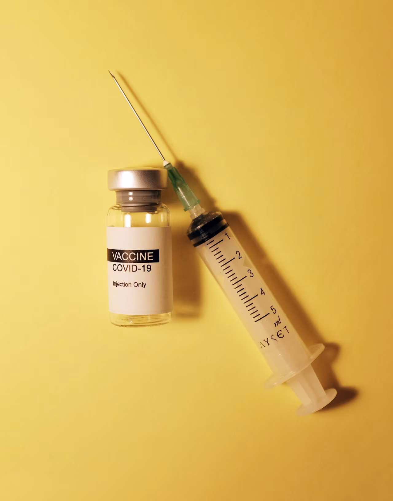 Injectievloeistof flesje met label vaccine covid-19 injection only naast injectiespuit met milliliter markeringen run op griepprik in twente